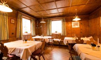 A cozy interior with wooden walls and tables dressed with white tablecloths. The windows have curtains, and small plants decorate the tables.