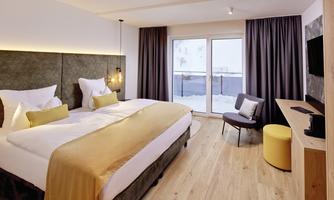 A modern hotel room with a large double bed and a cozy armchair. Large windows offer a view of the snowy landscape.