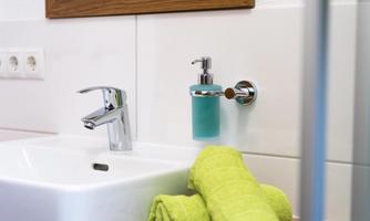 A modern sink with an elegant faucet and a soap dispenser. Two green towels are laid out on the shelf.
