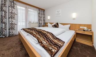 A cozy bedroom with a large bed and a big window. The walls are decorated with floral curtains, and there is a warm, inviting atmosphere.