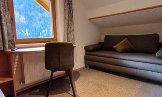A cozy room with a sofa and a desk. The window offers a view of nature.