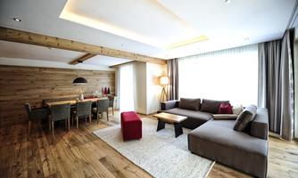 A modern living room with a cozy sofa and a dining area. The room is brightly lit and has wooden floors as well as large windows that let in plenty of daylight.