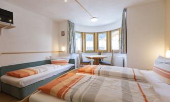A cozy room with two beds and a sofa bed. Large windows provide plenty of daylight and an inviting atmosphere.