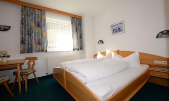 A bright room with a large bed and colorful curtains. There is a table with chairs and a window that lets in a lot of daylight.
