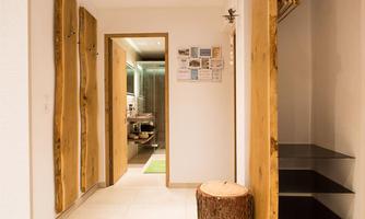A modern hallway with wooden elements and bright light. At the end of the hallway, a bathroom is visible and a green doormat is lying on the floor.