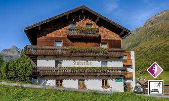 A traditional chalet in the mountains with wooden cladding and balcony flowers. Surrounded by green meadows and mountains.