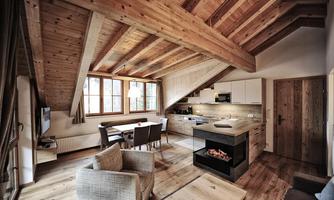 A modern living room with a wooden beam ceiling and large windows. The furnishings are cozy and inviting, with an open kitchen and a dining area.