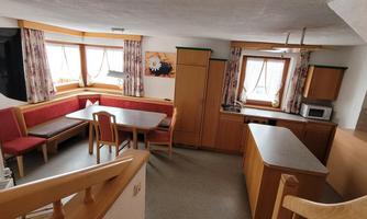 A bright apartment with a cozy seating area and a dining table. The kitchen is well-equipped and there are large windows for plenty of daylight.