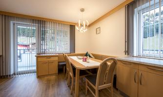 A bright dining room with a large table and several chairs. Large windows provide a view of the surroundings.