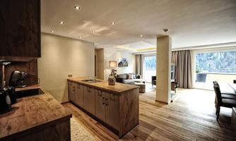 A modern, bright apartment with an open kitchen and a cozy living area. Large windows provide a view of nature and bring in plenty of daylight.