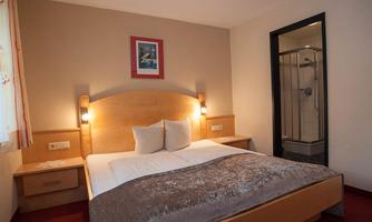 A cozy bedroom with a large bed and soft colors. In the background, there is an en-suite bathroom with a shower.