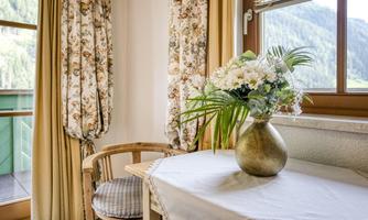 A cozy room with a wooden chair, a table, and a vase full of flowers. The windows show a beautiful view of the mountains.