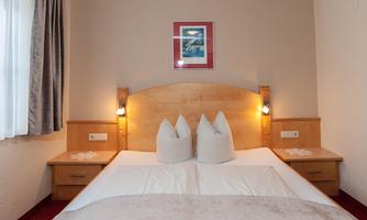 A cozy bedroom with a double bed and two pillows. Decorative pictures hang on the walls, and the lighting creates a warm atmosphere.