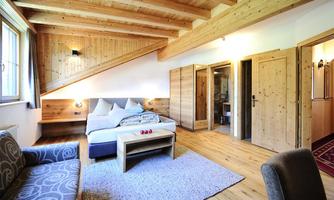 A cozy room with wooden ceilings and a large bed. The room is bright and inviting, with a soft carpet and a couch.