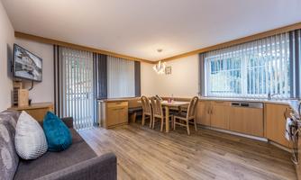 A modern living room with a gray sofa, a dining area, and large windows. The space is bright and friendly designed.