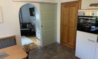 A modern room with an open kitchen and a dining area. In the background, you can see a living room with a cozy sofa.