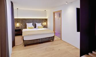 A modern hotel room with a large double bed and soft color tones. The wooden floor and stylish lighting create an inviting atmosphere.
