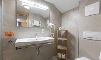 A modern bathroom with an elegant sanitary installation and a large mirror. A wooden shelf displays towels and toiletries.