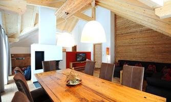 A modern, bright living-dining room with wooden ceilings and a large dining table. The decor is stylish with a fireplace and a cozy seating area.