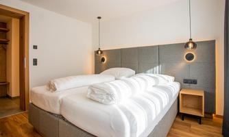 A modern bedroom with a large double bed and cozy cushions. The walls are bright and the wooden floors create a warm atmosphere.