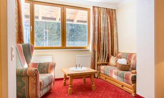 A cozy living space with a sofa and an armchair. Large windows let in plenty of light and provide a view outside.