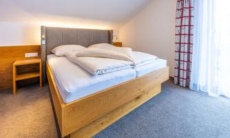 A cozy bedroom with a large double bed and a nightstand. The windows let in a lot of natural light.