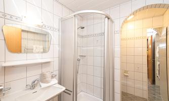 A modern bathroom with a shower, a sink, and a large mirror. The walls are covered in light tiles, and there is a warm atmosphere.