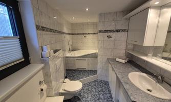 A modern bathroom with a bathtub, a shower, and a sink. The walls are brightly tiled and the fittings are functional and stylish.