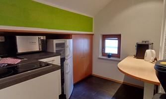 A modern kitchen with a stove, refrigerator, and a small dining area. The walls are designed in fresh colors, including a green accent.