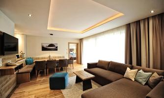 A modernly furnished living room with a cozy sofa and a dining table. Large windows provide plenty of daylight and a welcoming atmosphere.