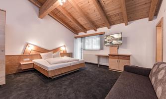 A modern room with wooden ceilings and a large bed. There is a flat-screen TV and a comfortable sofa.
