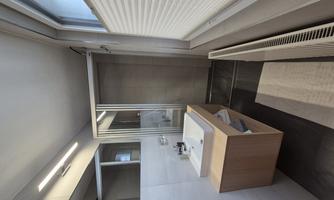A modern bathroom with a sink on a wooden shelf and a separate shower. The walls are bright and the windows let in plenty of daytime light.