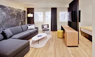 A modern living room with a large gray sofa and an elegant coffee table. The walls are plain, and the room has plenty of daylight.