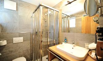 A modern bathroom with a shower and a glass partition. The space is furnished with gray tiles and wooden details.