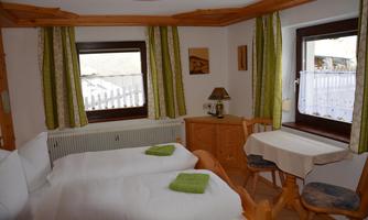 A cozy room with two beds and bright wooden interiors. Large windows let in plenty of light, and a small table invites you to linger.