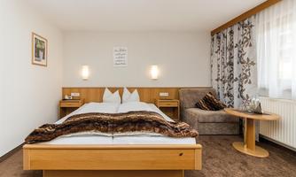 A cozy hotel room with a double bed and a comfortable armchair. Bright colors and simple furniture create an inviting atmosphere.