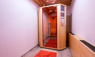 A modern designed wellness area with a wooden infrared cabin. The floor is covered with a red carpet and the walls are in subtle colors.