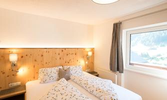 A cozy bedroom with a large bed and wooden paneling. The window offers a view of the surrounding landscape.