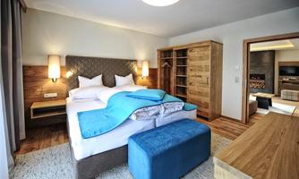 A modern bedroom with a large bed and wooden paneling. There is a cozy stool and ample storage space in the closet.