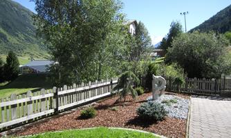 A beautiful garden landscape with various plants and a graceful sculpture. In the background, the mountains and a clear sky are visible.