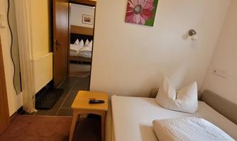 A cozy room with two beds and a small table. A picture of a flower hangs on the wall, and in the background, more beds are visible.