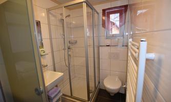 A modern bathroom with a shower and a sink. The wall tiles are light and the room is well lit.