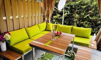 A cozy outdoor seating area with bright green cushions and a wooden table. Surrounding it is a beautiful garden with visible plants.