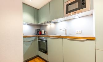 A modern kitchen with green cabinets and wooden countertops. It is well-lit and includes an oven as well as practical appliances.