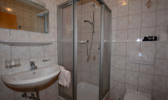 A modern bathroom with a shower and a sink. The walls are tiled, and a mirror hangs above the sink.