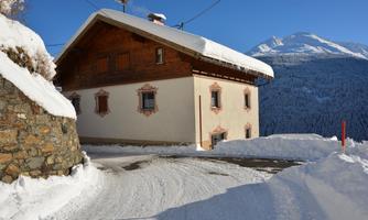 A traditional house in the mountains, surrounded by freshly fallen snow. The sky is clear and blue.