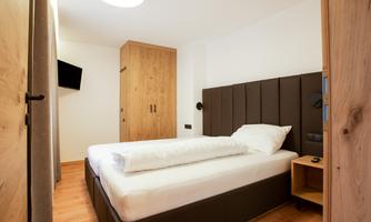 A modern bedroom with a large bed and wooden furniture. A television is mounted on the wall and the atmosphere is bright and inviting.