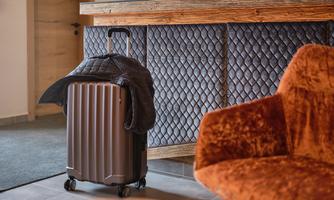 A suitcase stands next to a modern hotel reception. In the foreground, an orange armchair is visible.