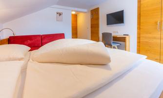 A modern room with a double bed and a red couch. There is a desk and a television on the wall.