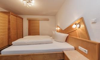 A cozy bedroom with wooden furniture and a large bed. The walls are bright and the room is well-lit.